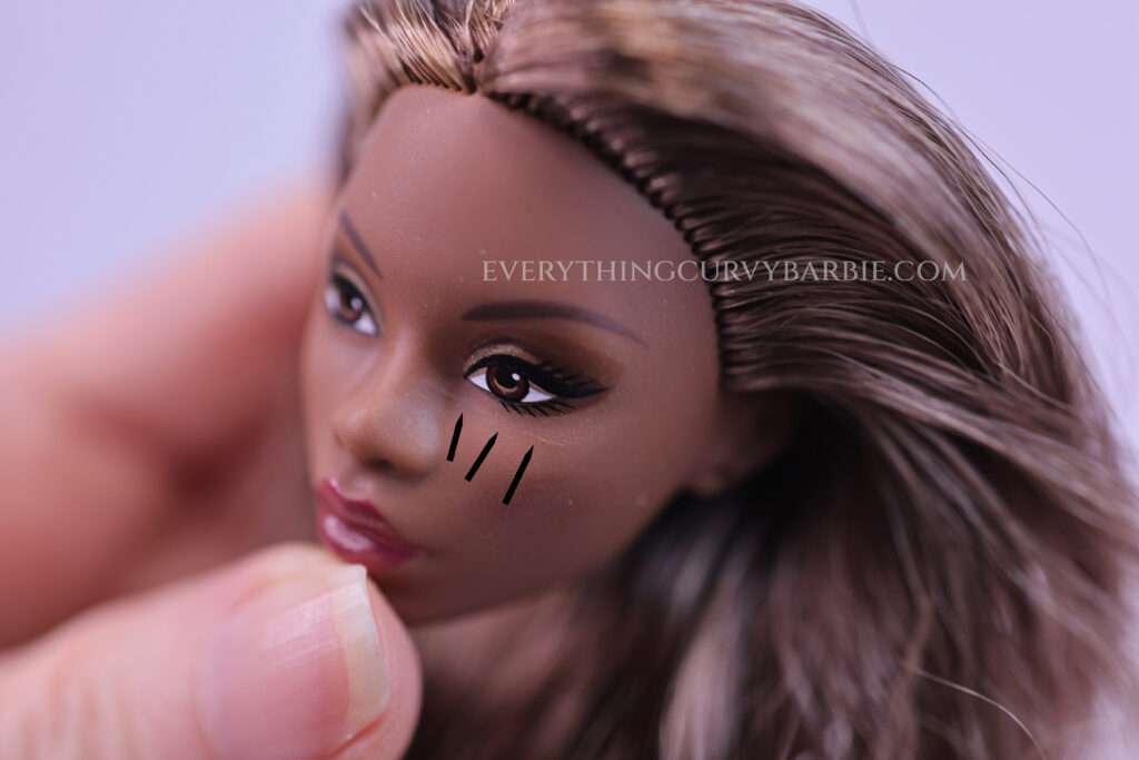A small bright white paint risk is clearly visible just under the doll’s right eye of Barbie Basics 09 2026